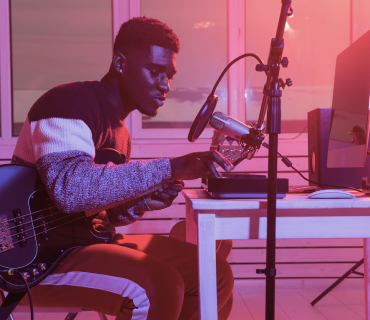 Record Vocals Man sitting by a desk, holding a guitar and singing into a microphone