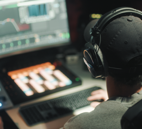 Step 1: Compile material A view of the back of a person wearing a baseball cap and overear headphones, sitting in front of a screen with an open music program.